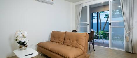 A modern living room with a brown sofa, a small white table with a remote control, and a potted orchid.
