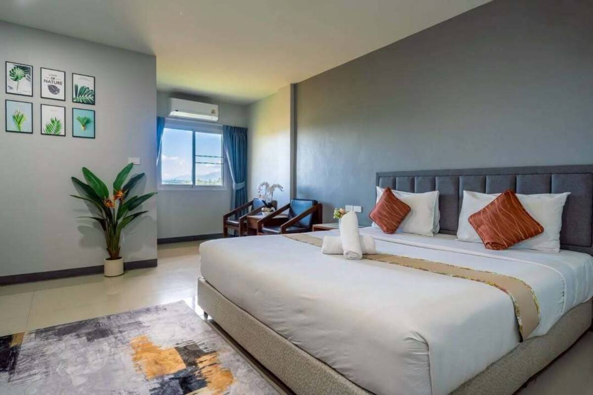A hotel room with a large bed, a desk, a chair, a potted plant, and framed pictures on the wall.