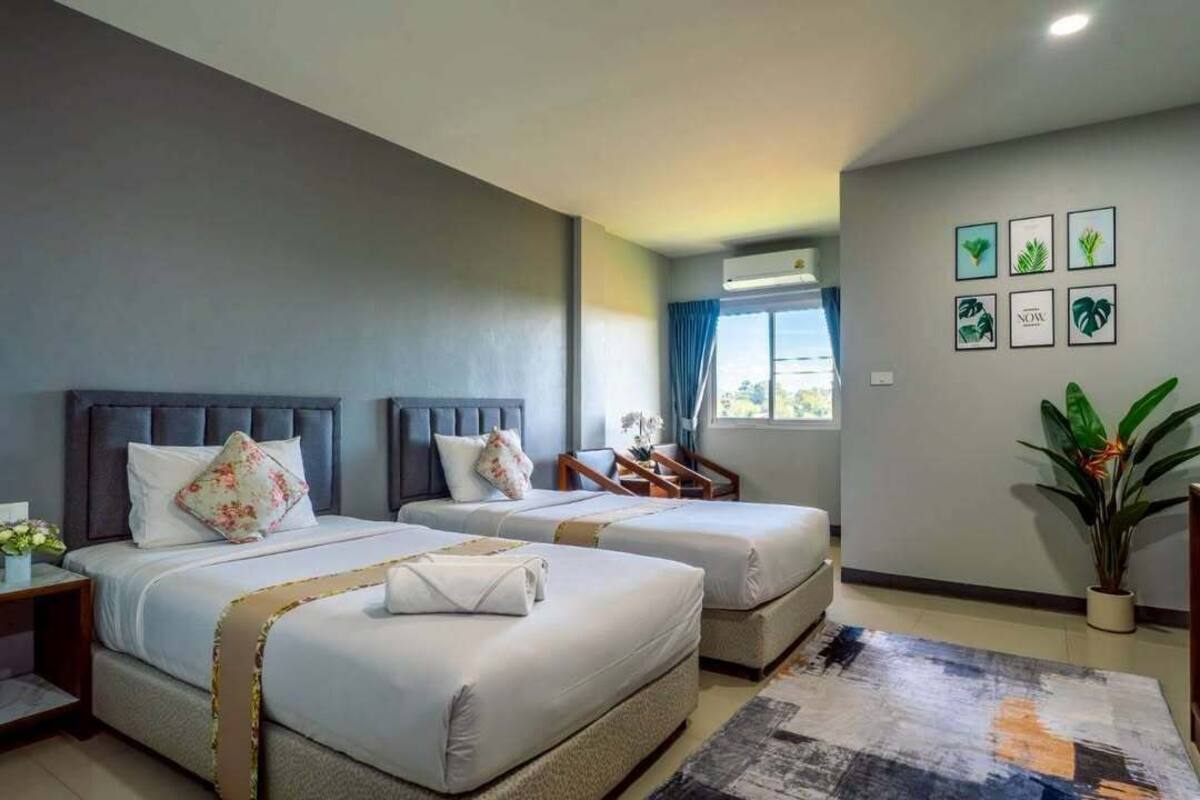 A hotel room with two beds, a desk, a chair, a potted plant, and a window with curtains.