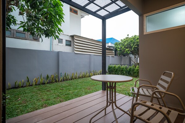 Un patio con mesa y sillas, un espacio con césped y una pared blanca con ventanas.