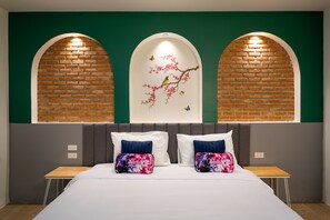 Habitación de hotel con una cama, dos mesitas de noche, una pared verde con diseño de ladrillos y un mural de pájaros sobre una rama.