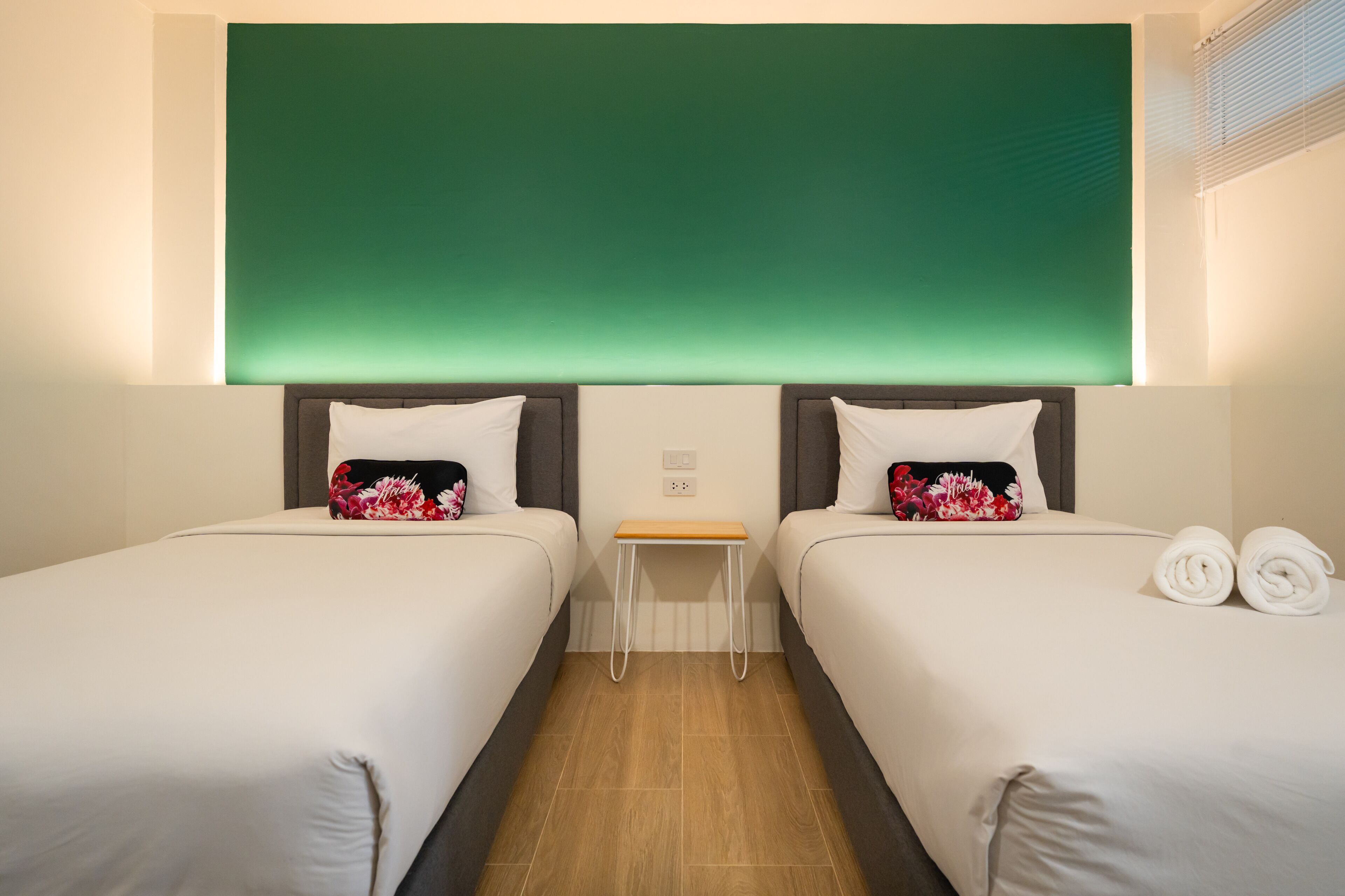 Habitación de hotel con dos camas, una mesita pequeña y una pared verde decorativa.