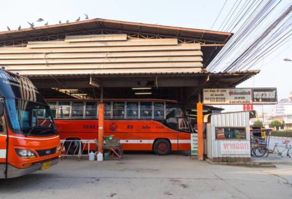 Una parada de autobús con refugio, un autobús rojo y un pequeño quiosco.