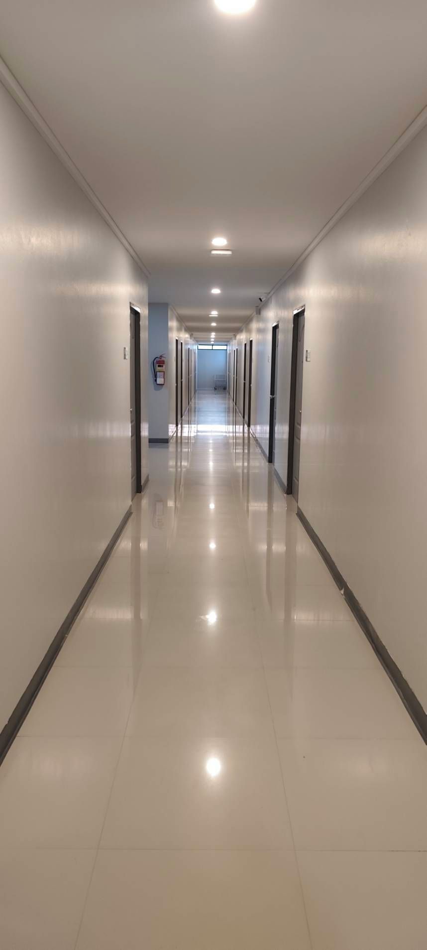 A long, narrow hallway with white walls and a shiny tiled floor.