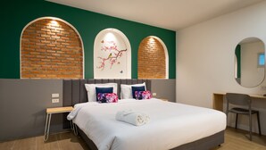 A modern hotel room with a large bed, a desk, and a chair. There are two arched brick walls with a floral mural. - KYP Hotel (Fang)