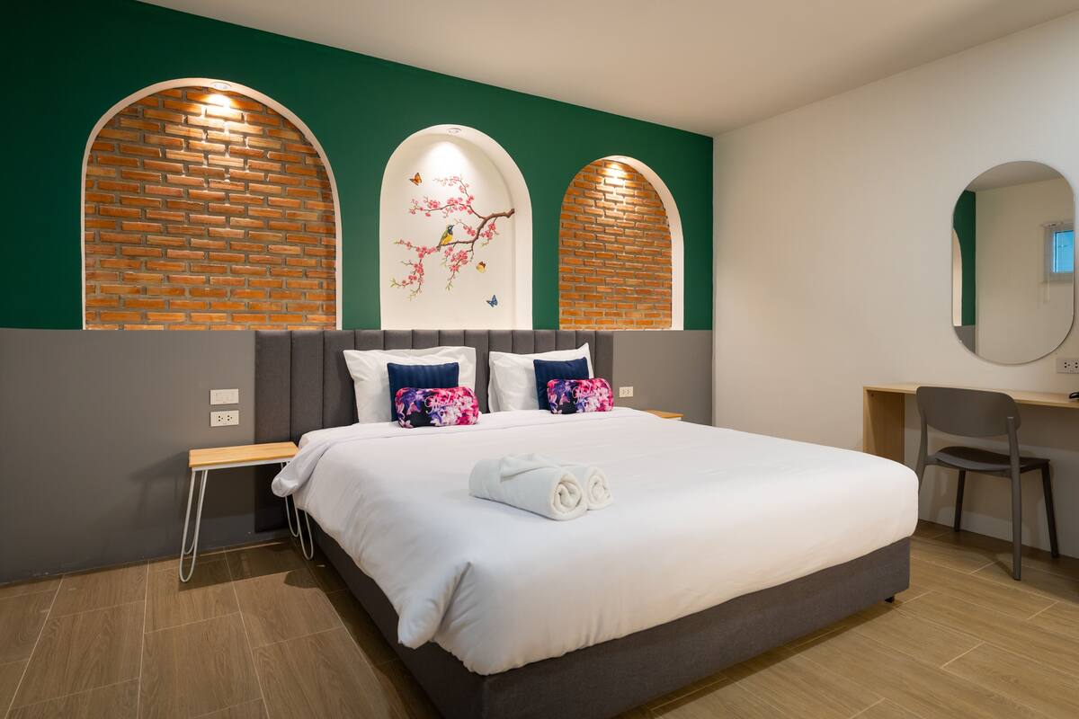A modern hotel room with a large bed, a desk, and a chair. There are two arched brick walls with a floral mural.
