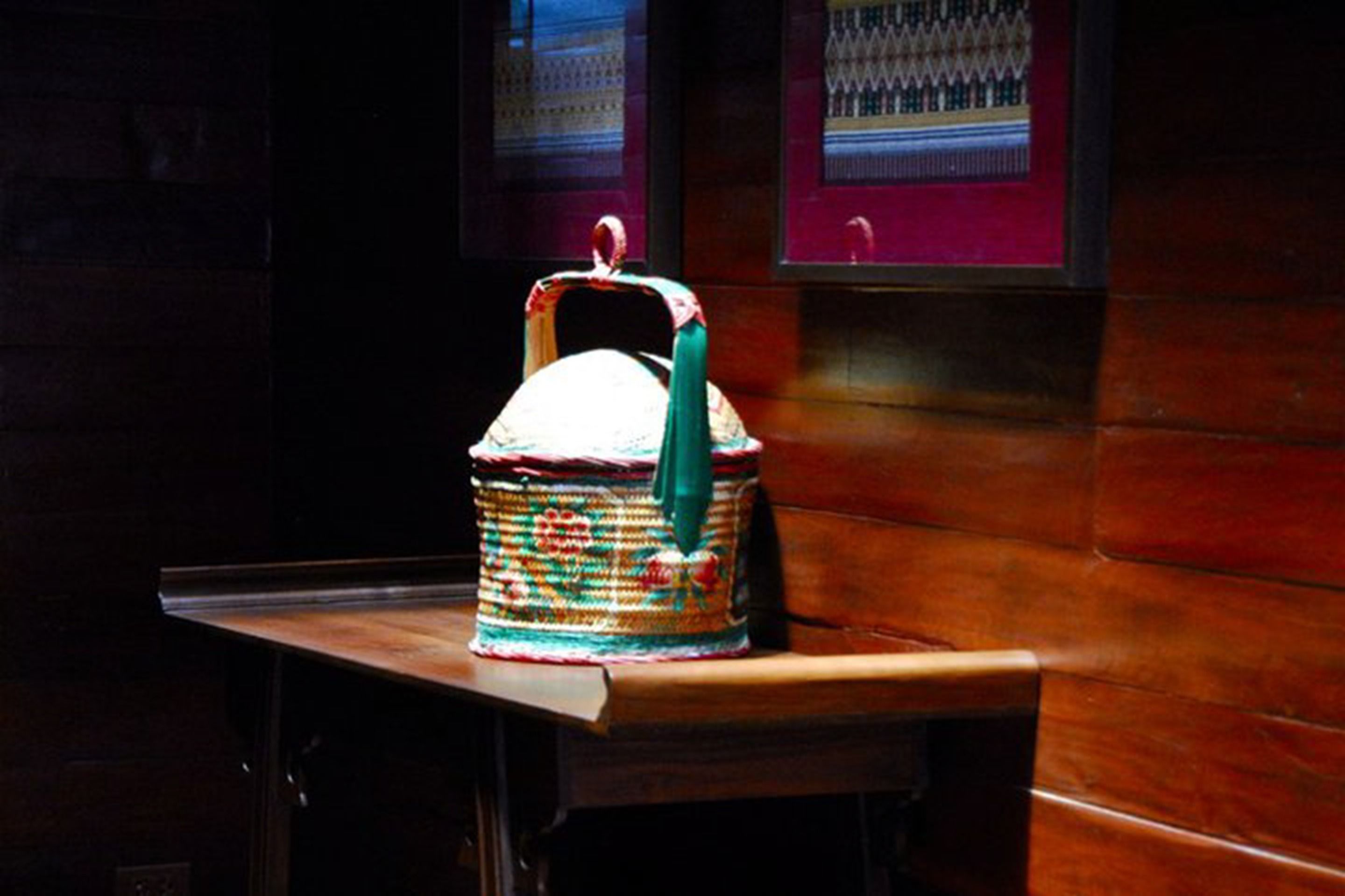 Un cesto di vimini con un manico su un tavolo di legno in una stanza scarsamente illuminata con carta da parati decorata.