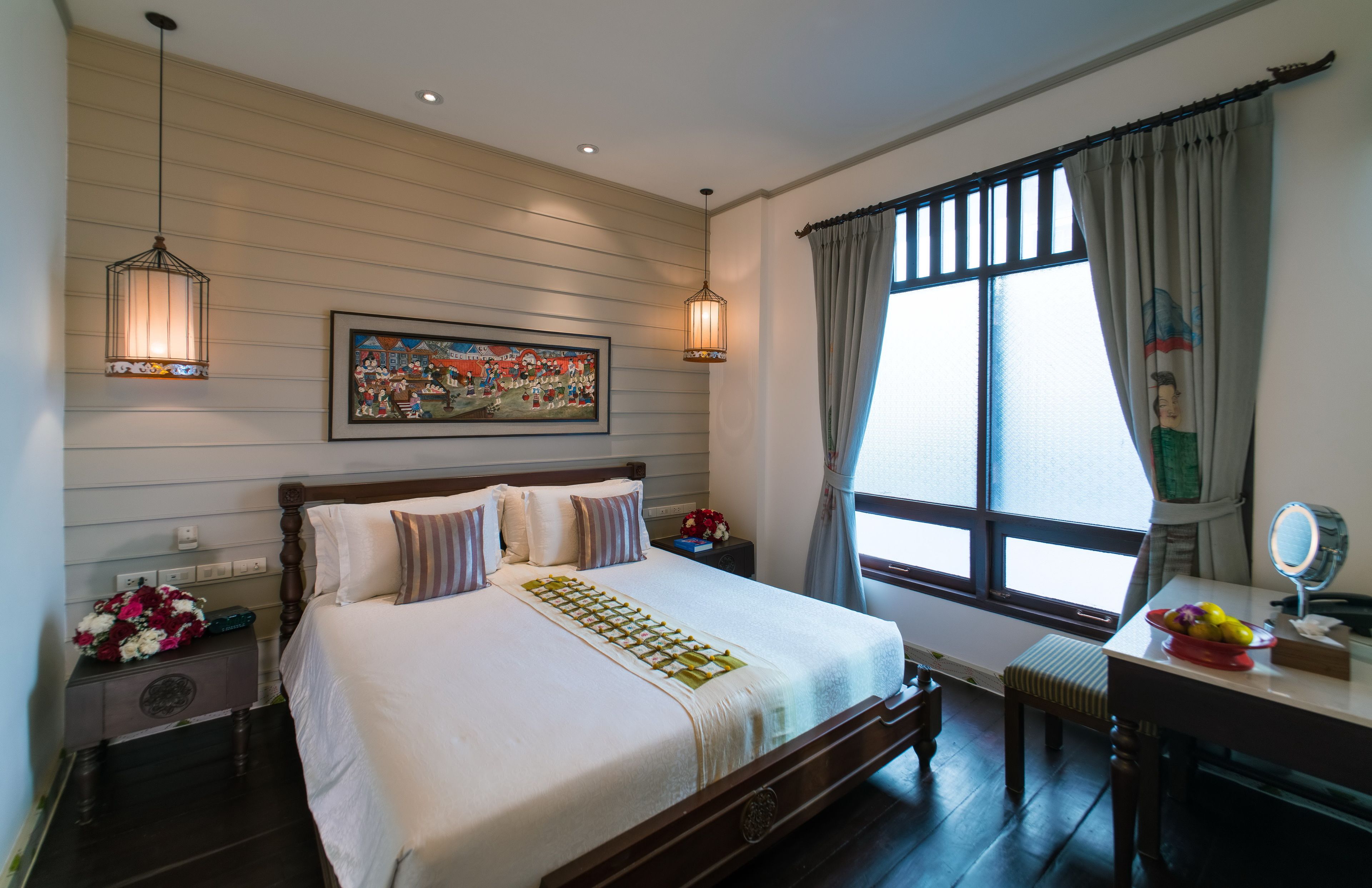 A neatly arranged bedroom with a large bed, bedside tables, a desk with a mirror, and a window with curtains.