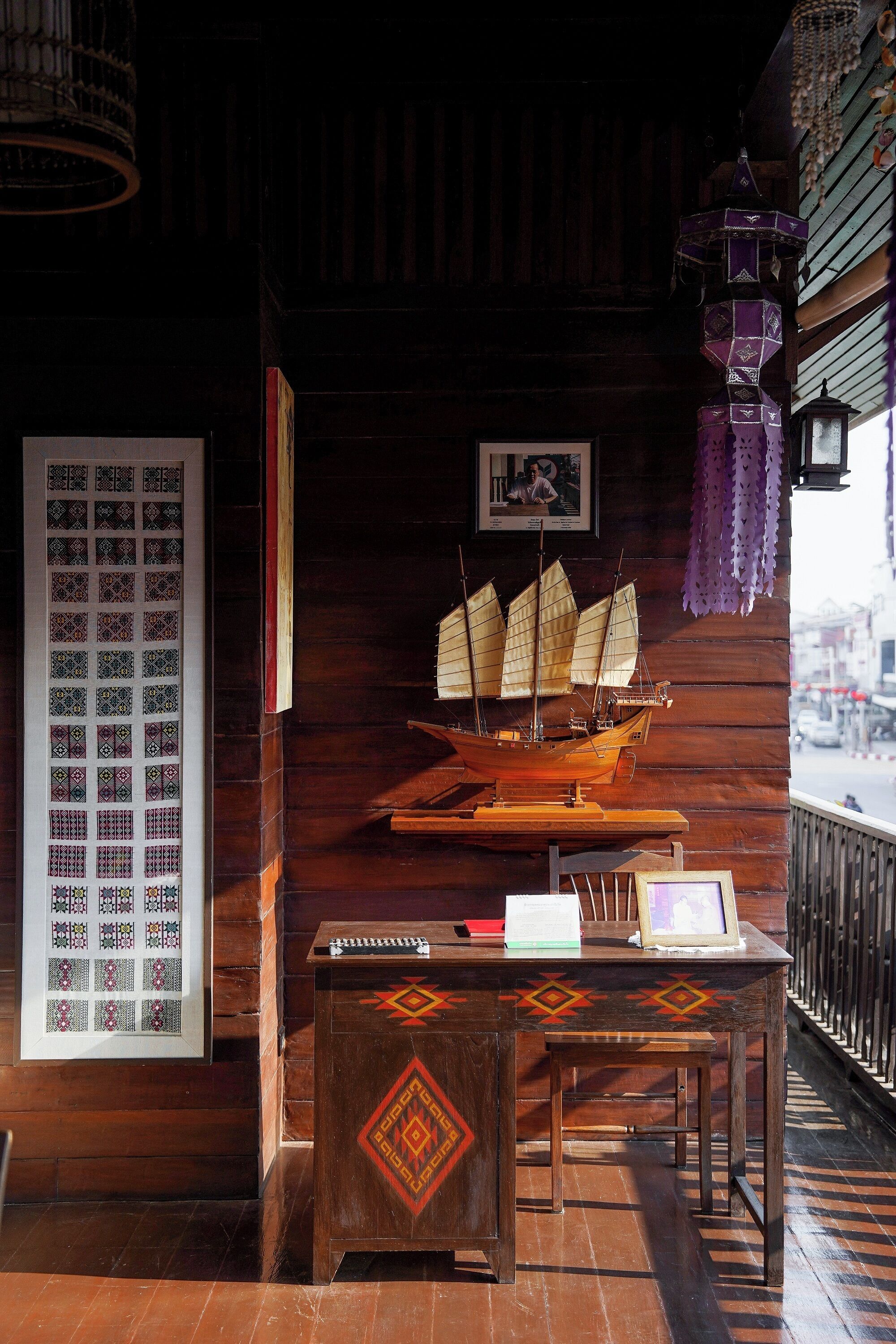 A wooden interior with a model ship, a framed picture, and a patterned wall hanging.