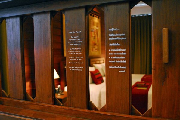 A wooden partition with a mirror reflecting a room. The partition has text on it, likely providing information about the room or hotel. - Pukha Nanfa Hotel (Nan)