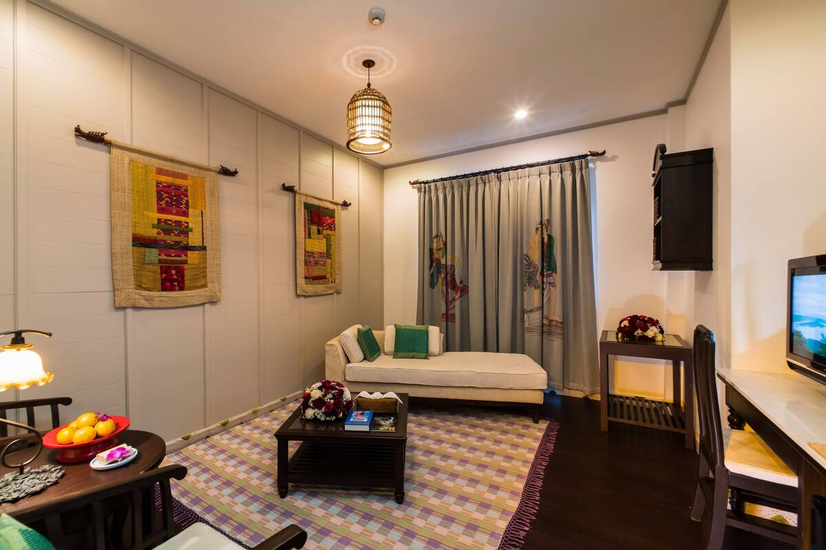 A cozy hotel room with a bed, a small coffee table, a TV, and a decorative wall hanging.