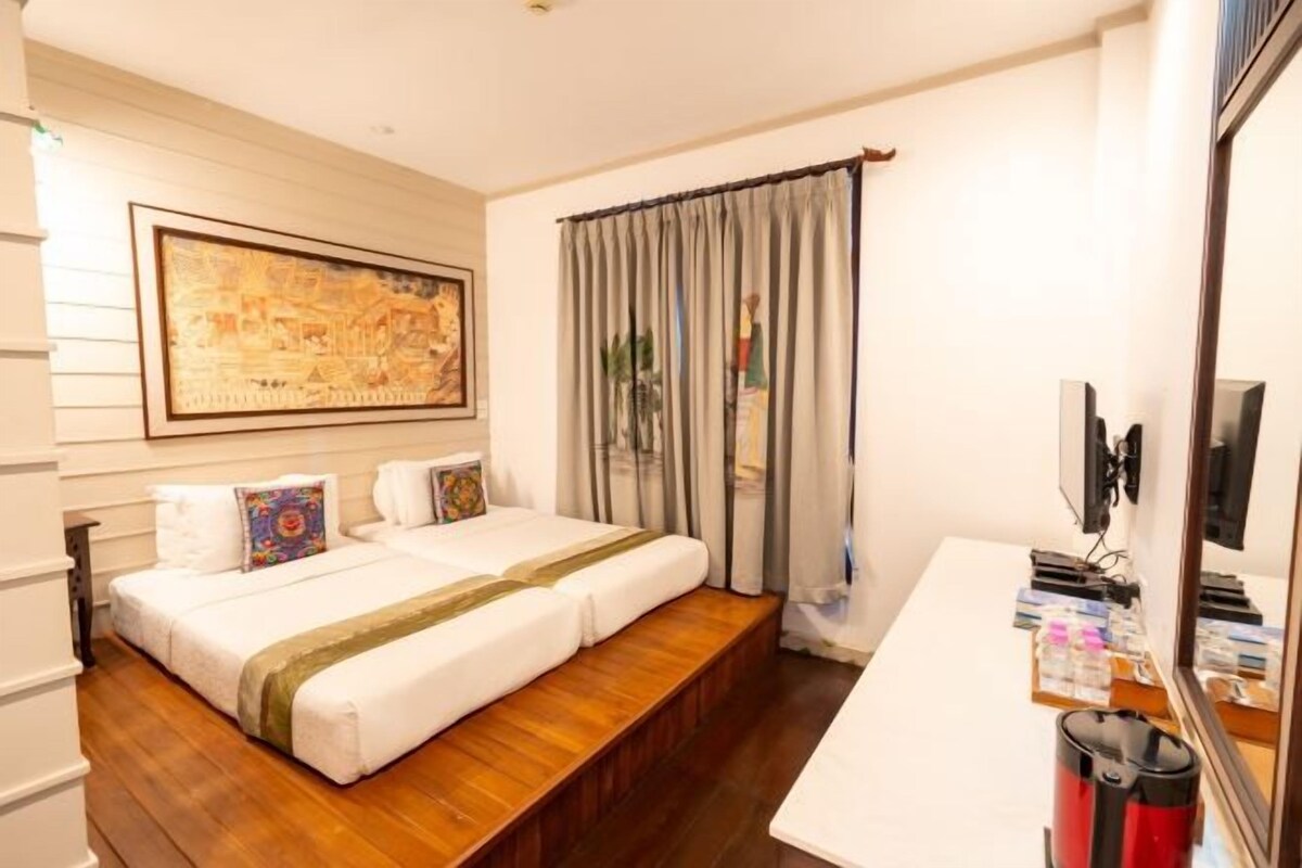 A hotel room with a bed, a desk, a television, and a painting on the wall.