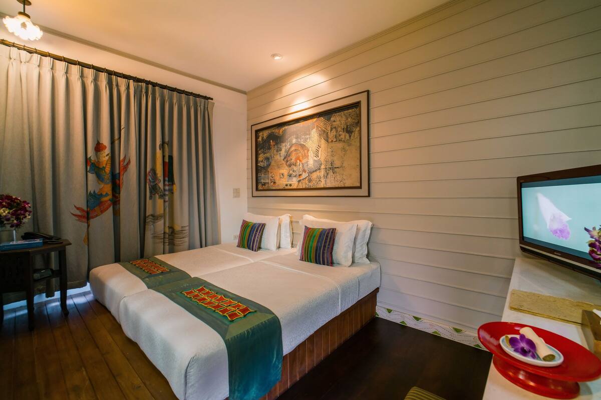 A hotel room with a bed, a television, a painting on the wall, and a desk with a vase of flowers.