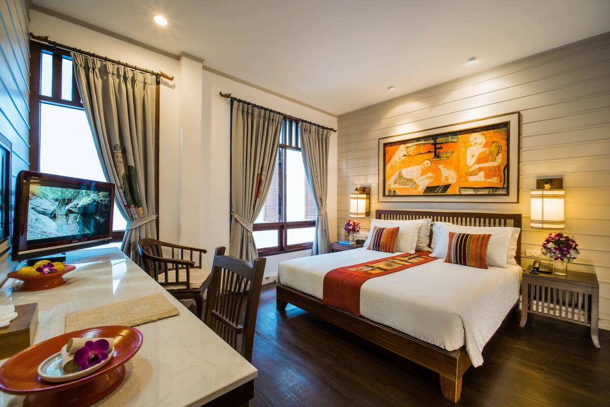 A hotel room with a large bed, a desk with a computer, a chair, and a window with curtains.