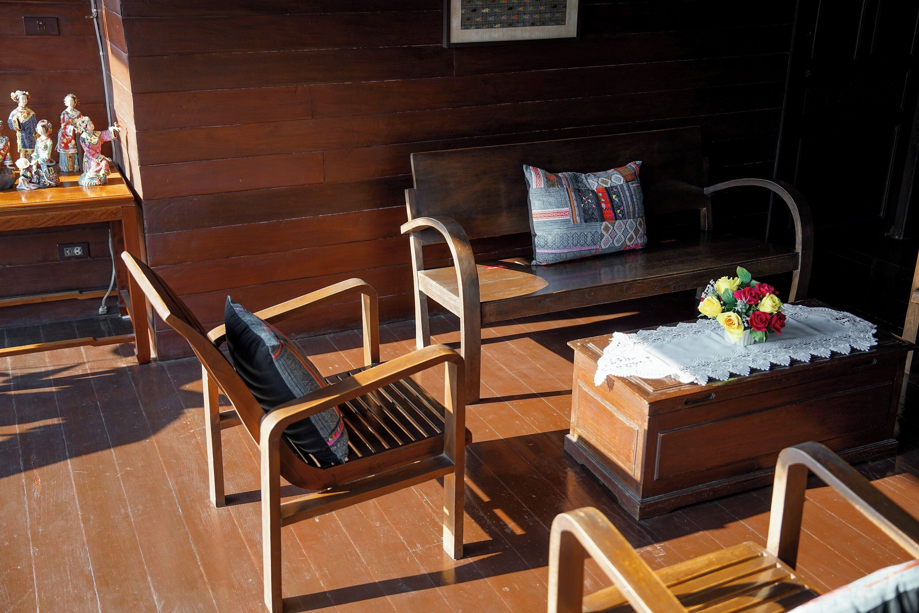 Un banco de madera con cojín, una mesita con mantel de encaje y flores, y un aparador de madera.