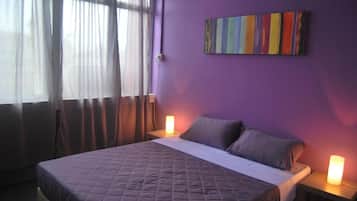 A bedroom with a bed, two bedside tables, a wall-mounted air conditioner, and a window with curtains.