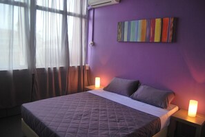 A bedroom with a bed, two bedside tables, a wall-mounted air conditioner, and a window with curtains.