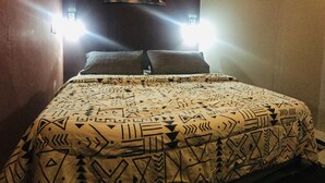 A bed with a patterned bedspread, two wall-mounted lights, and two wall decorations. - Borneo Seahare Guesthouse - Hostel (Kuching)