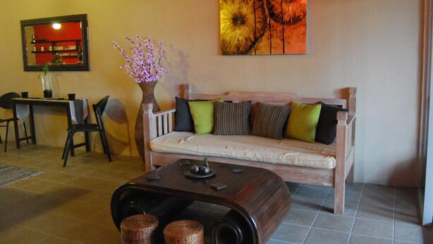 A living room with a sofa, a coffee table, a vase with flowers, a painting on the wall, and a dining area in the background. - Borneo Seahare Guesthouse - Hostel (Kuching)