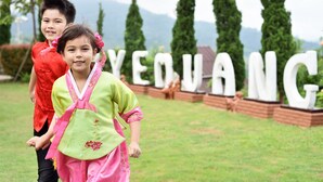 Two children in traditional attire walking in front of a sign with the word "YEVANG". - Byemuang Khaokho Resort View Talaymok (Khao Kho)