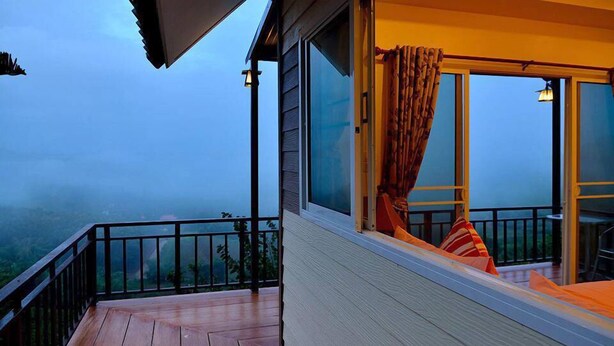 A balcony with a wooden floor, large windows with curtains, and a view of a mountainous landscape. - Byemuang Khaokho Resort View Talaymok (Khao Kho)