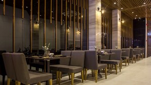 A modern restaurant with long tables and cushioned chairs, featuring vertical wooden slats and ambient lighting.