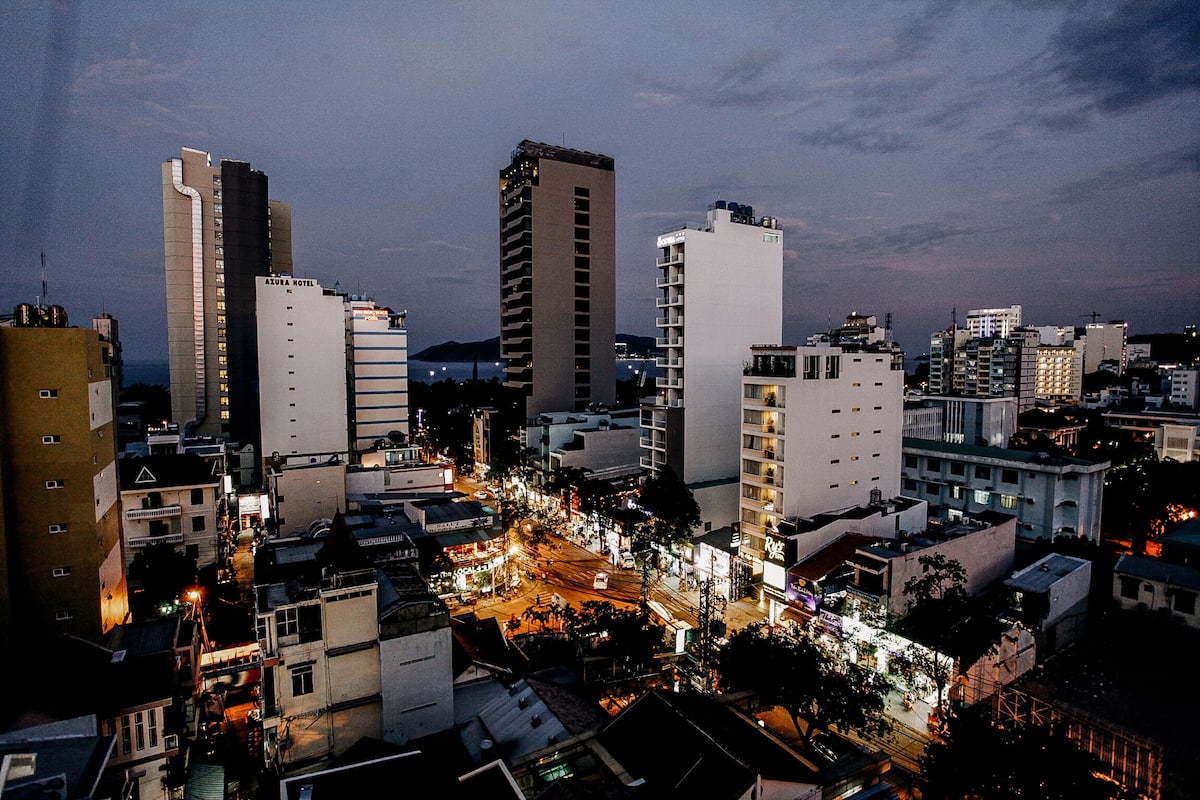 Une vue sur une ville au crépuscule, avec de hauts immeubles, dont un hôtel à plusieurs étages doté de balcons.