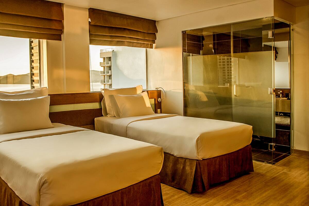 Une chambre d’hôtel avec deux lits, une douche à parois de verre et une vue sur les montagnes.