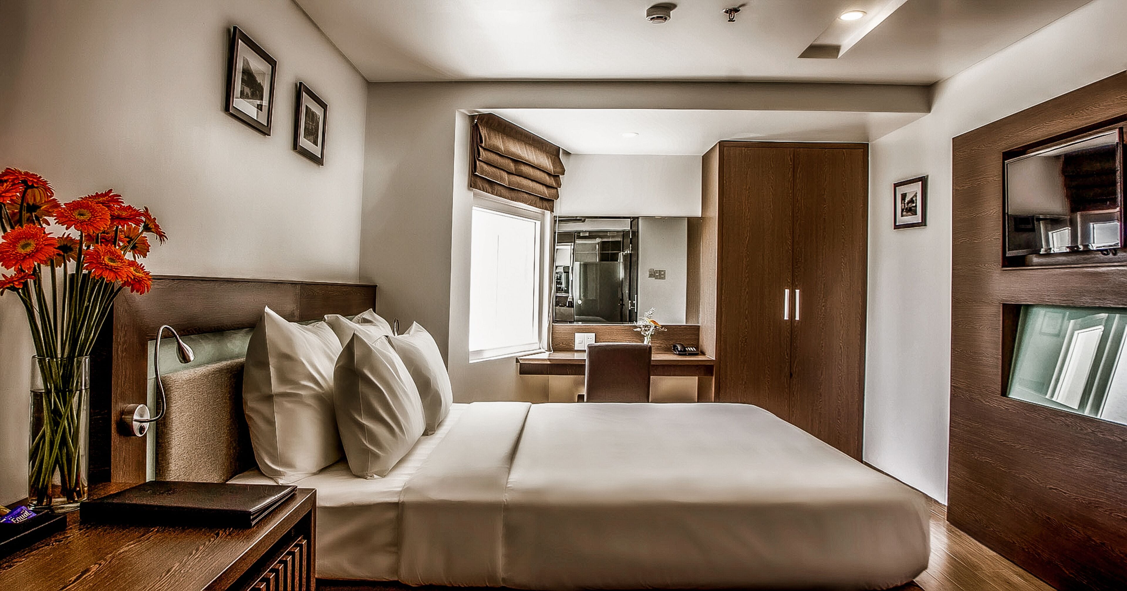 A modern hotel room with a large bed, a desk, and a wardrobe.