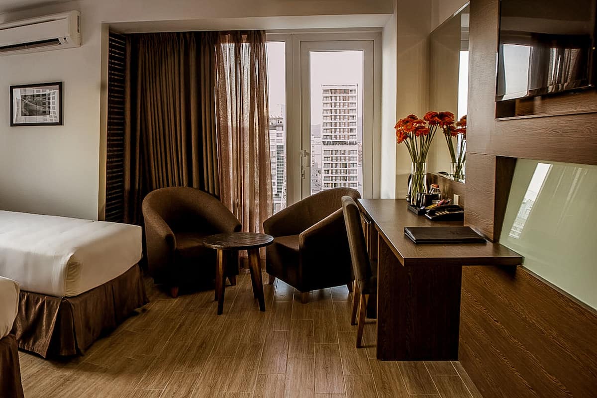Une chambre d’hôtel avec deux lits, un bureau, une chaise, une fenêtre donnant sur la mer et un tableau au mur.