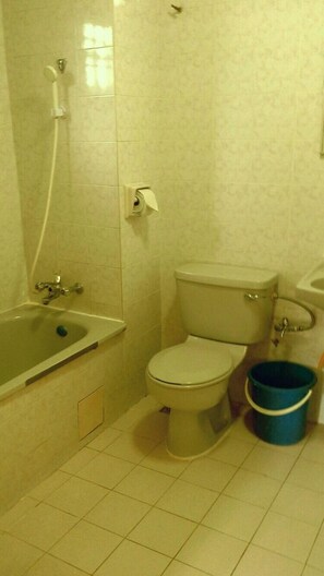 A bathroom with a bathtub, toilet, and a bucket.
