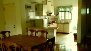 Una cocina con una mesa y sillas de madera, un refrigerador y una ventana con cortinas.