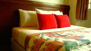 Una cama con cabecera de madera, colcha con estampado geométrico y dos almohadas, una roja y otra blanca.