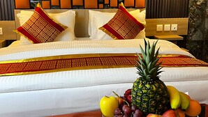 Une chambre d’hôtel avec un lit, un panier de fruits sur la table de chevet et un mur orné d’un motif géométrique.