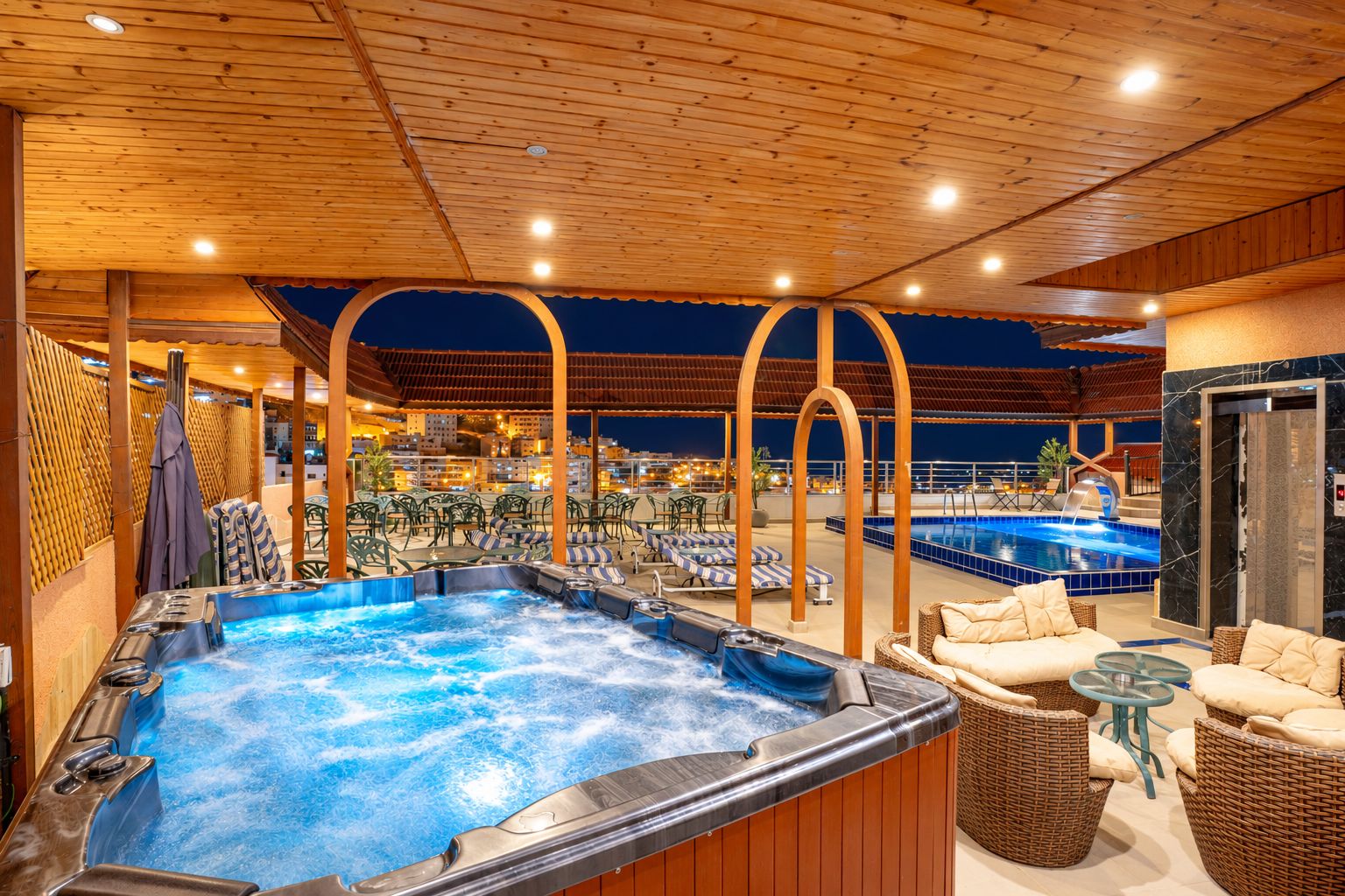 Zona de hidromasaje con asientos y piscina, techo de madera y mobiliario de exterior.