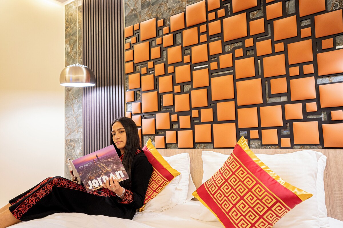 A person sitting on a bed with a patterned wall behind them, holding a book.