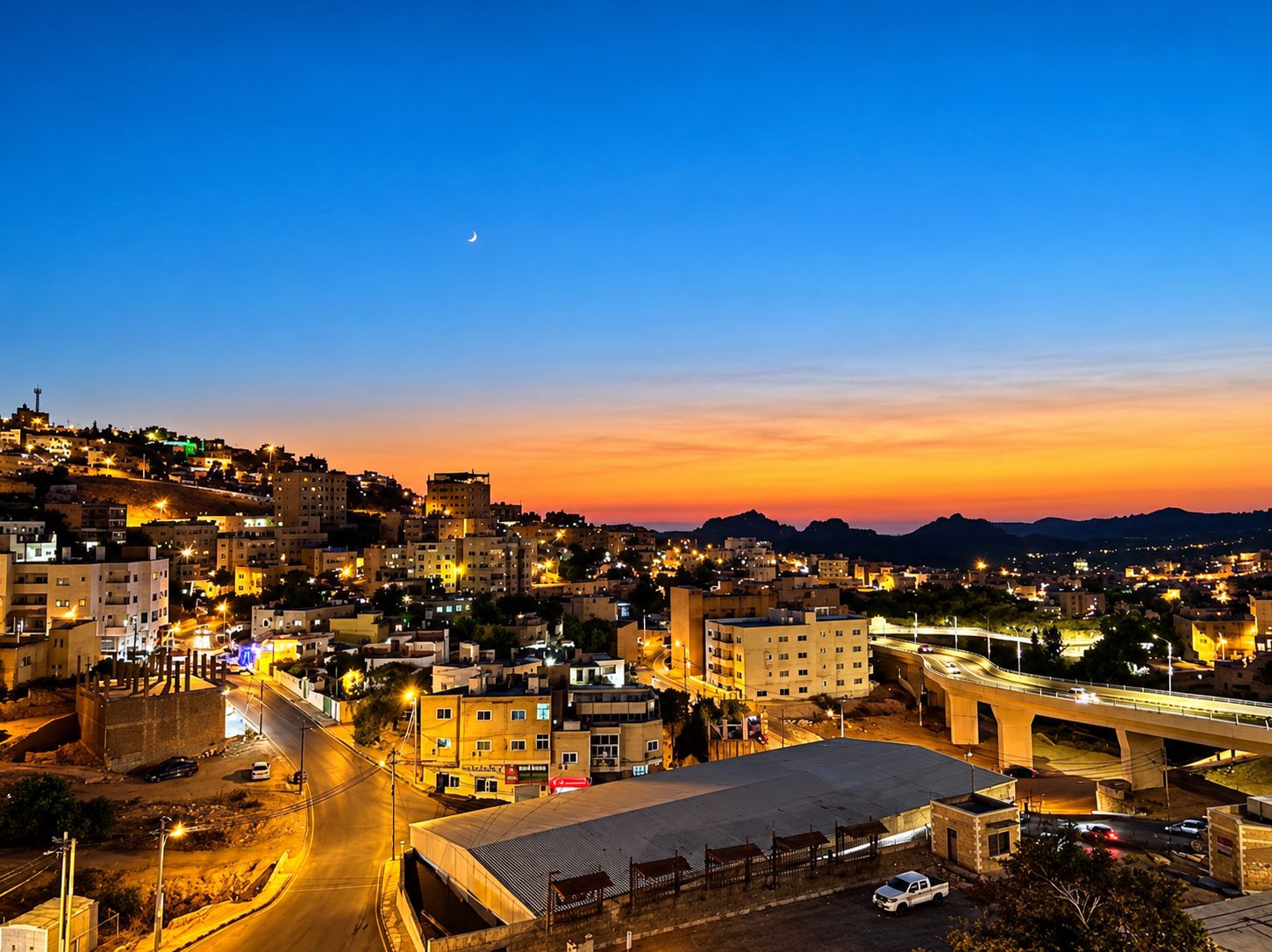 A cityscape at dusk with illuminated buildings and a bridge.