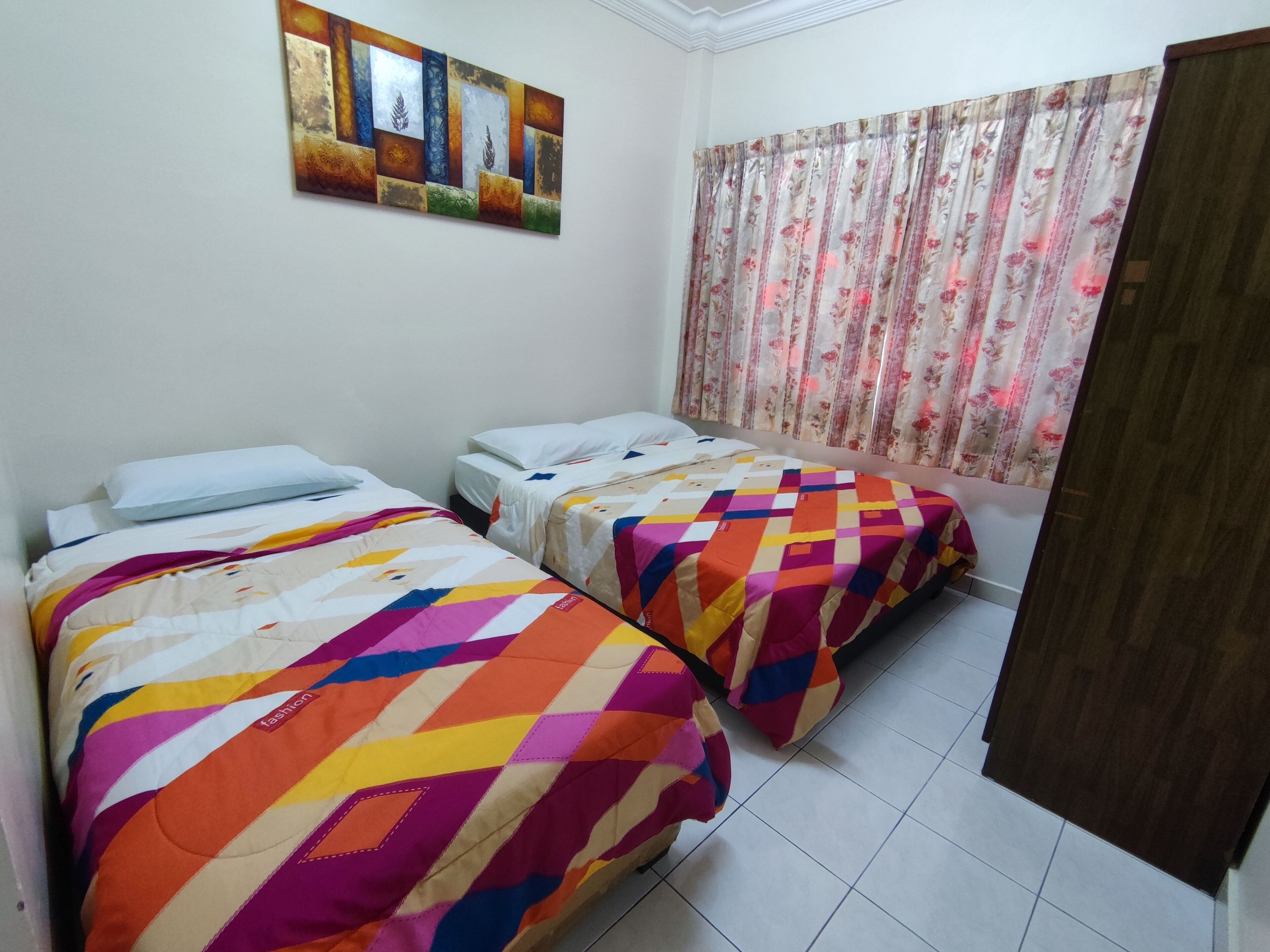 Ein Zimmer mit zwei Betten, jeweils mit farbenfroher Bettwäsche, einem blumigen Vorhang und einem Bild an der Wand.