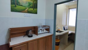 A kitchen with wooden cabinets, a coffee maker, and a sink. There is a painting of a forest on the wall. - KPW at Royal Lily Apartment (Tanah Rata)