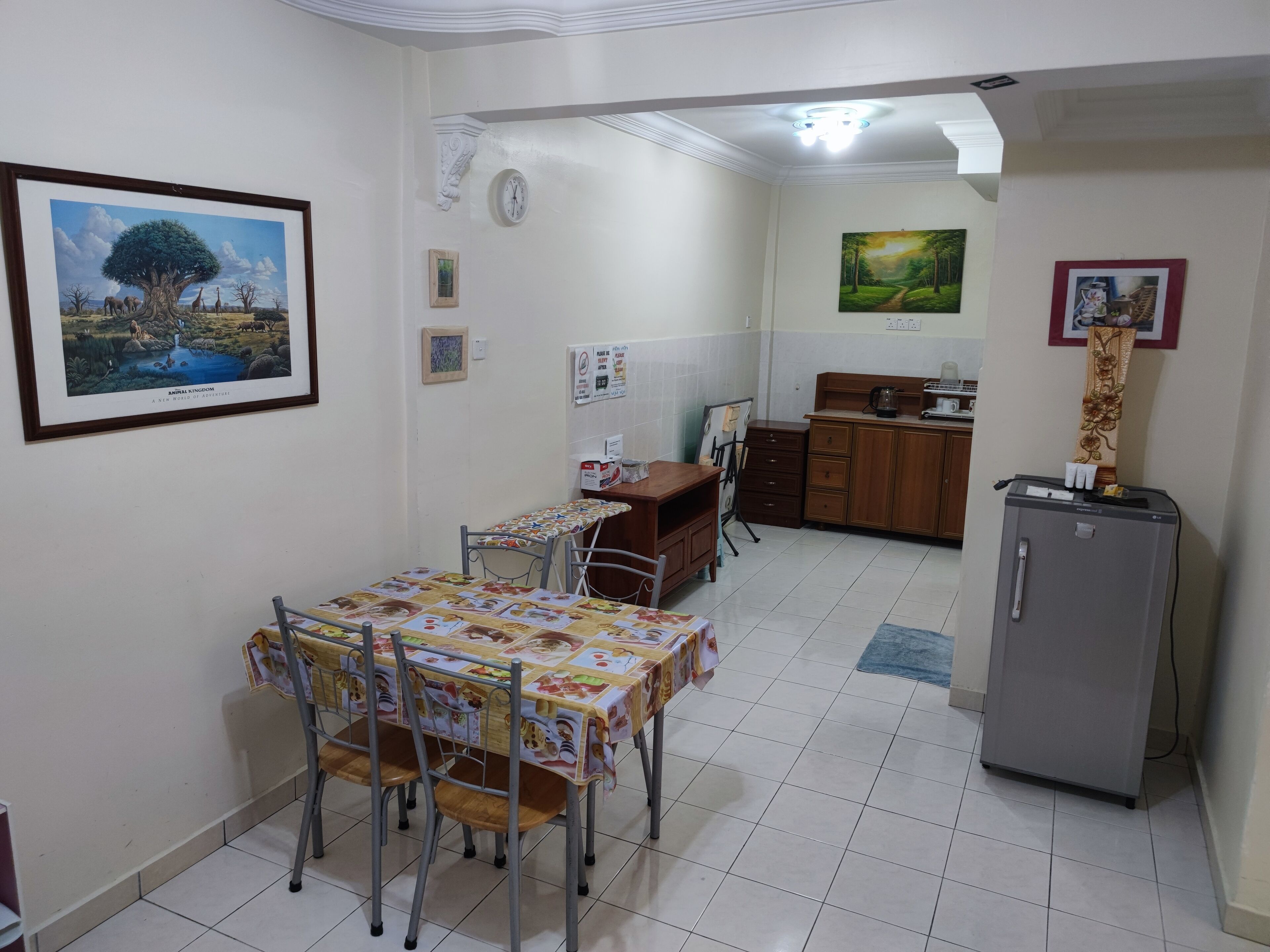 A dining area with a table set for four, a refrigerator, and a kitchen area in the background.