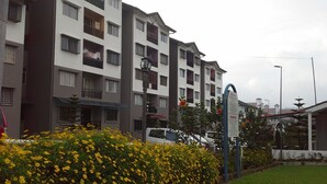 A multi-story residential building with balconies, a signpost with a warning sign, and a garden with yellow flowers. - KPW at Royal Lily Apartment (Tanah Rata)