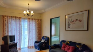 A living room with a sofa, armchair, wooden coffee table, and a television on a stand. - KPW at Royal Lily Apartment (Tanah Rata)