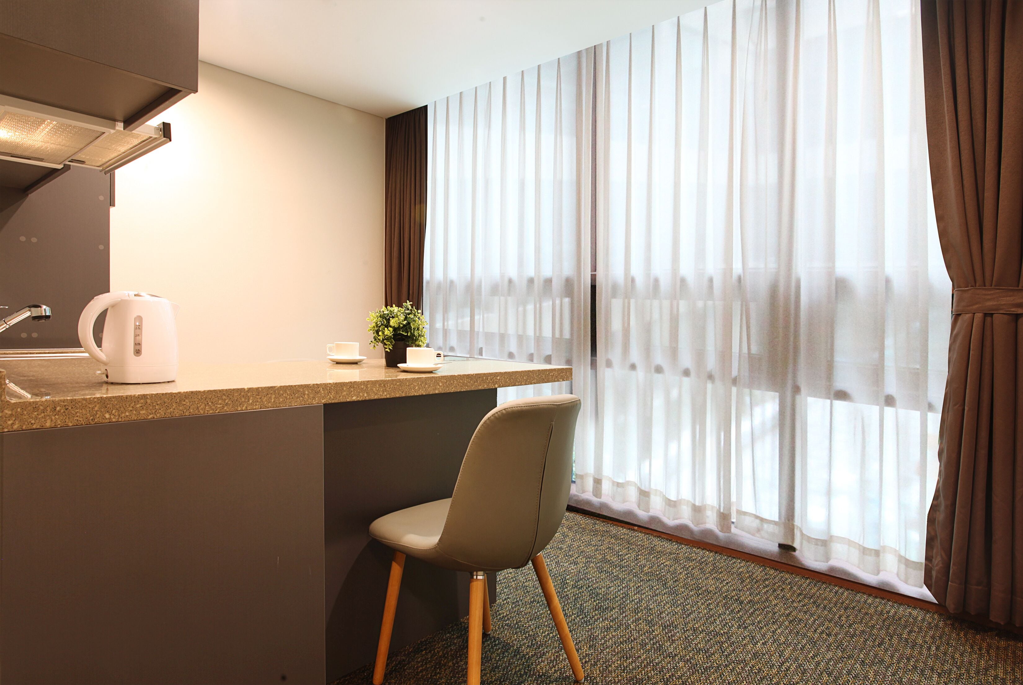 Une chambre d’hôtel dotée d’une kitchenette, d’un coin repas et d’une grande fenêtre avec des rideaux légers.