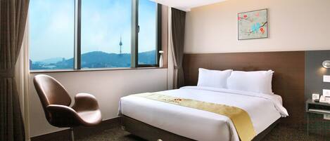 Habitación de hotel con una cama grande, una silla, una mesita de noche y vistas a un paisaje urbano a través de amplios ventanales.