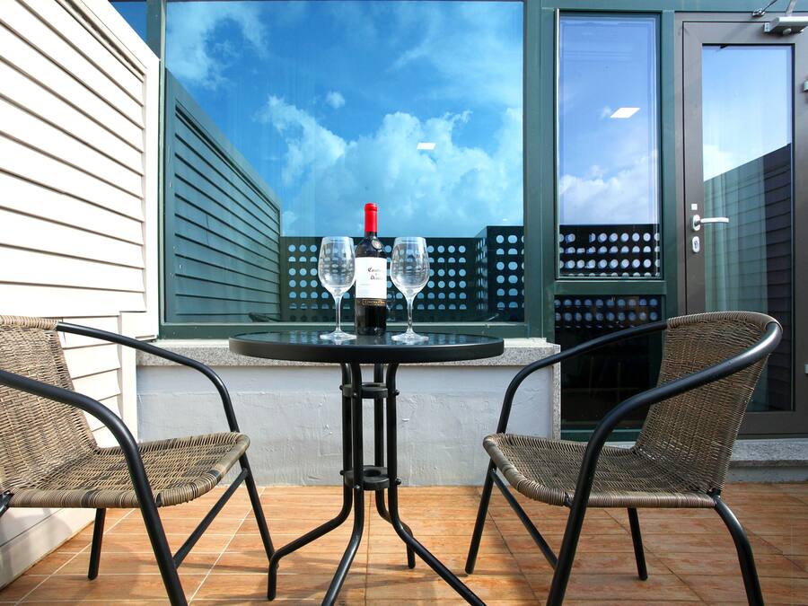 Eine Terrasse mit zwei Korbstühlen, einem Tisch und einer Weinflasche.