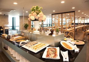 Un bufé con diversos platos, un gran centro de mesa floral y una zona de estar con sillas y mesas de madera.