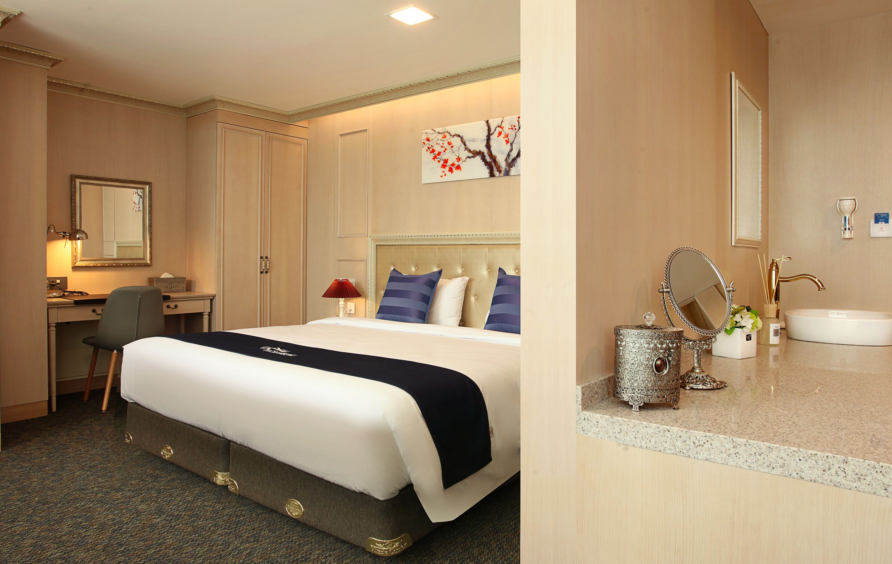 A hotel room with a large bed, a desk, a chair, a dresser, a mirror, and a bathroom with a sink and a toilet.