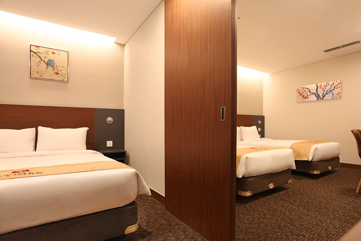 Hotellihuone, jossa on kaksi sänkyä, puinen pääty ja yöpöytä sekä seinälle ripustettu taulu.