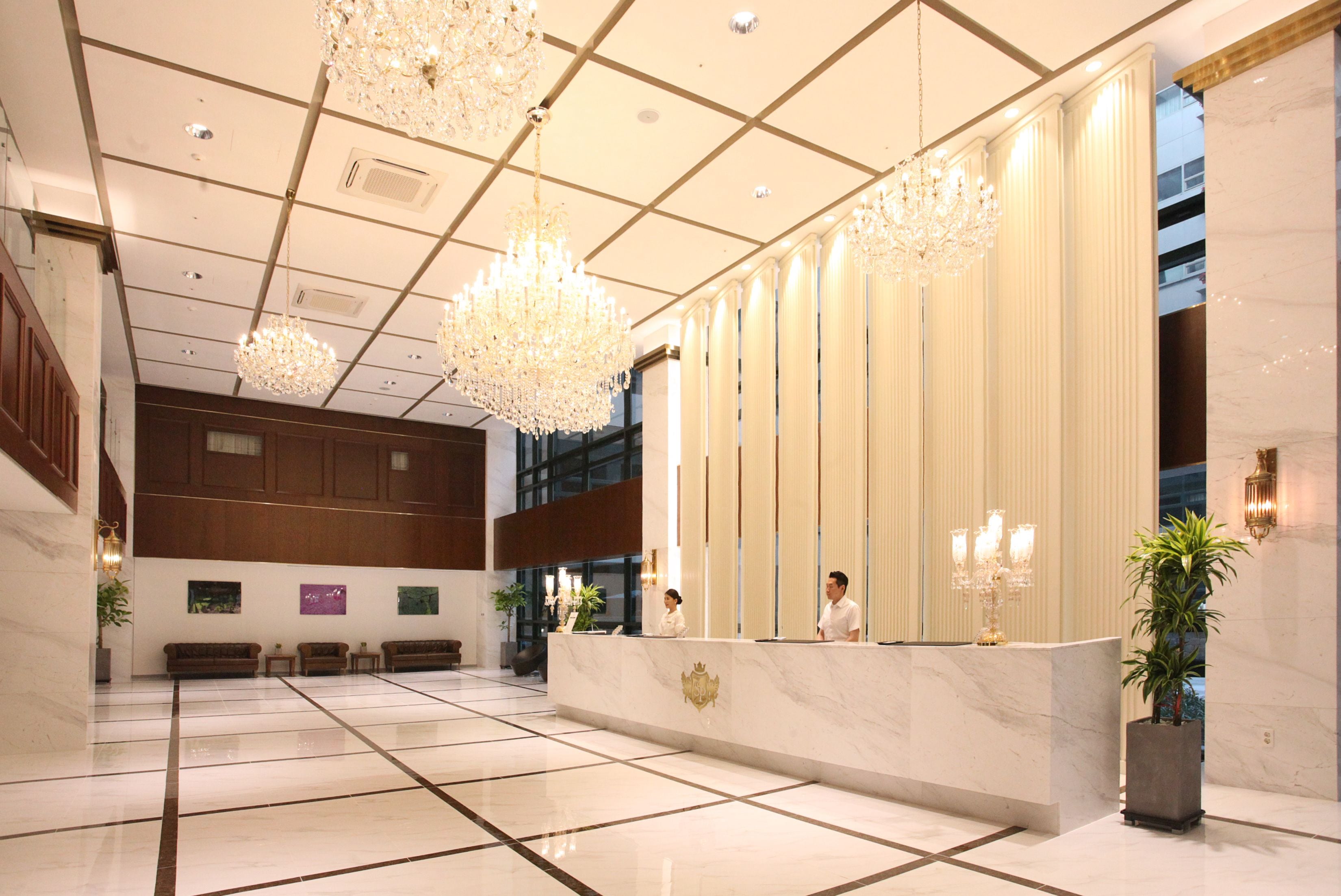 Um hall amplo com piso de mármore, balcão de recepção e lustres elegantes.