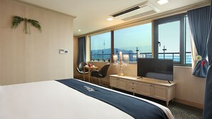 A hotel room with a large bed, a desk with a TV, a chair, and a view of a cityscape through large windows. - Hotel Skypark Kingstown Dongdaemun (Seoul)